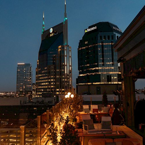 Rooftop view of a cityscape at dusk with illuminated buildings and cozy seating on the terrace for relaxation.