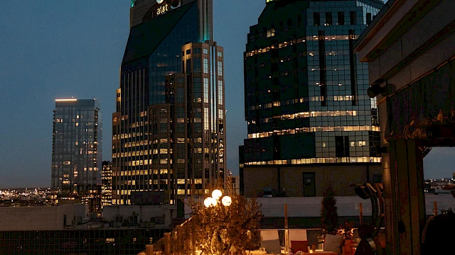 Rooftop view of a cityscape at dusk with illuminated buildings and cozy seating on the terrace for relaxation.