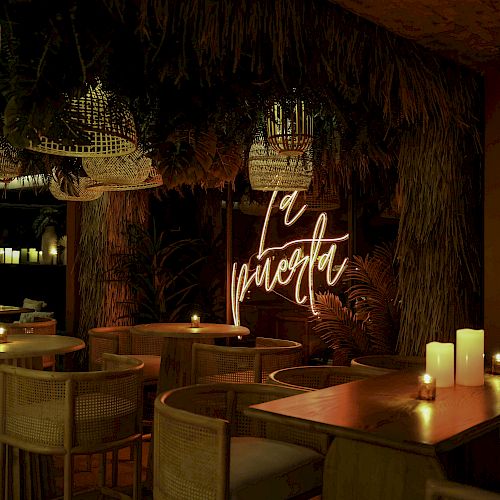 A dimly lit restaurant with wooden tables, wicker chairs, and candles. Neon sign reads 
