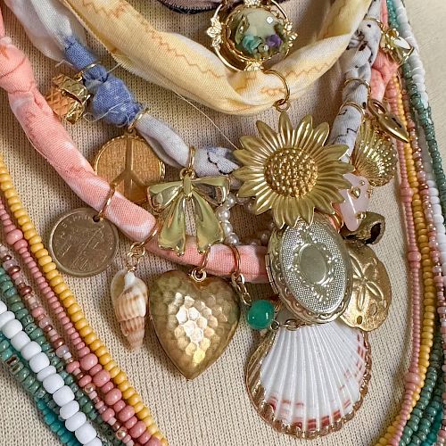 A collection of colorful beaded necklaces with assorted pendants including a sunflower, shell, and heart on display.