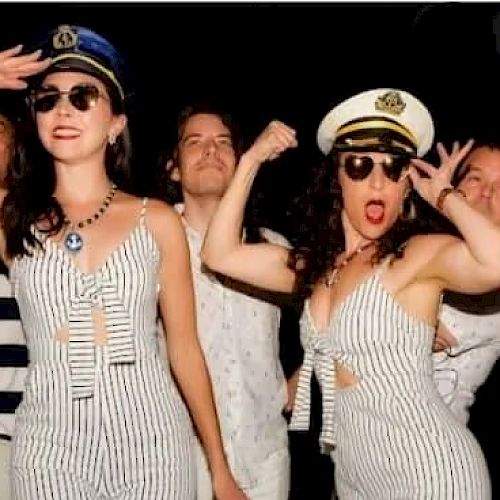 People in sailor-themed outfits strike playful poses, wearing captain hats and striped attire, exuding a lively and festive atmosphere.